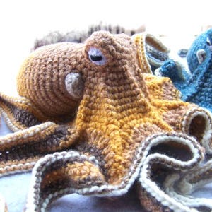 May include: A crocheted octopus plush toy with brown, yellow, and white yarn. The octopus has eight tentacles and a large head with large eyes.