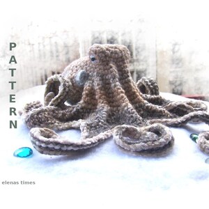 May include: Crocheted octopus amigurumi toy with brown and white yarn. The octopus is lying on a white surface with a blue and green glass bead nearby. The text "CROCHET PATTERN" is visible on the left side of the image.