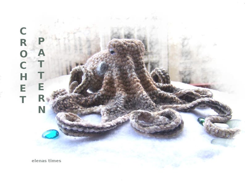May include: Crocheted octopus amigurumi toy with brown and white yarn. The octopus is lying on a white surface with a blue and green glass bead nearby. The text "CROCHET PATTERN" is visible on the left side of the image.