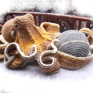 May include: A crocheted octopus with brown, yellow, and white yarn. The octopus has eight tentacles and a round head. The octopus is sitting on a white surface.