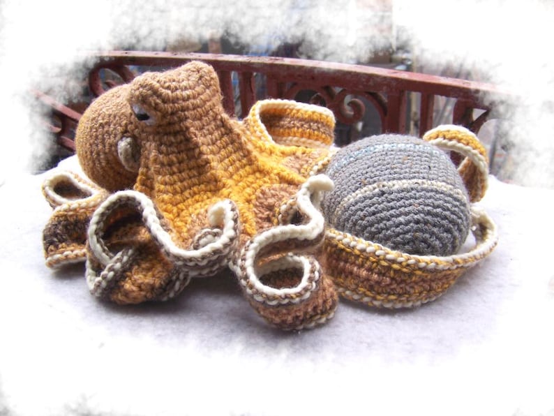 May include: A crocheted octopus with brown, yellow, and white yarn. The octopus has eight tentacles and a round head. The octopus is sitting on a white surface.
