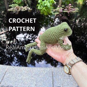May include: A green crocheted frog amigurumi with dark eyes and textured yarn stitches. The text CROCHET PATTERN and RealAmigurumiAndMore are visible on the image. The frog has a rounded body, four limbs with small toes, and a light-colored belly.