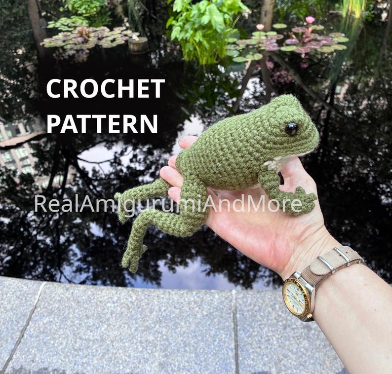 May include: A green crocheted frog amigurumi with dark eyes and textured yarn stitches. The text CROCHET PATTERN and RealAmigurumiAndMore are visible on the image. The frog has a rounded body, four limbs with small toes, and a light-colored belly.