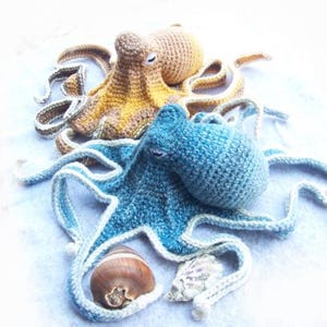May include: Two crocheted octopus plushies, one blue and one yellow, with white accents. The blue octopus has a shell and a seashell next to it.