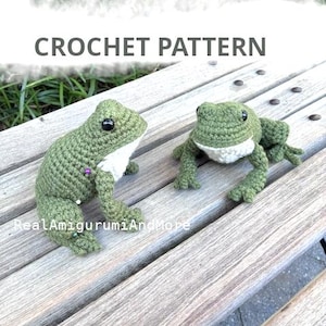 Può includere: Due rane all'uncinetto fatte a mano con corpi verde oliva e pance bianche, dotate di occhi in plastica nera. Il testo CROCHET PATTERN e RealAmigurumiAndMore è visibile. Le rane sono realizzate con un motivo a maglia testurizzato.