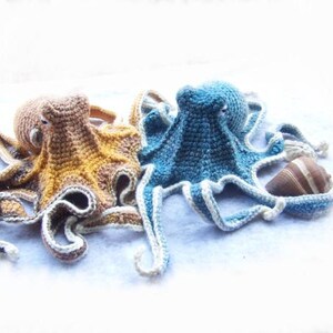 May include: Two crocheted octopus plushies, one blue and one brown, with a brown seashell.