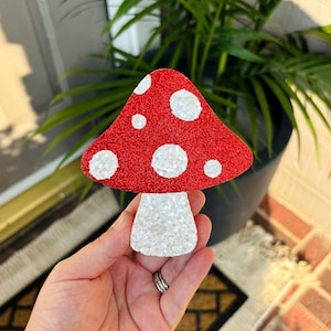 May include: A red and white glitter mushroom with white polka dots. The mushroom is made of felt and has a sparkly finish.