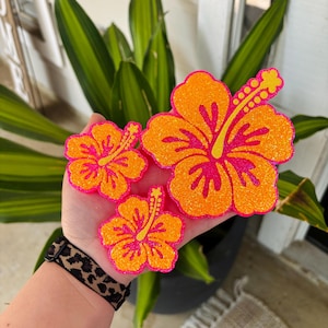 May include: Three pink and orange glitter hibiscus flower decorations. The largest flower is about 5 inches wide.