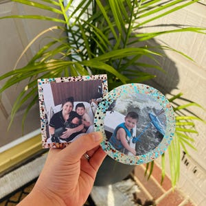 May include: Two resin photo coasters with glitter accents. One coaster features a family photo of a woman and two children. The other coaster features a photo of a boy in a life jacket on a boat.
