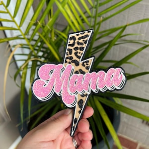 May include: Pink glitter "Mama" text on a black lightning bolt with a leopard print design.