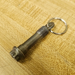 May include: A silver metal bolt keychain with a threaded shaft and a hexagonal head. The bolt is attached to a silver metal key ring.