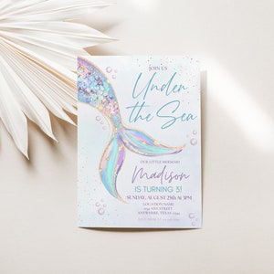 May include: A light blue and purple mermaid tail with gold glitter accents on a white background. The text "Join Us Under the Sea" is written in blue script. The text "Our Little Mermaid Madison is Turning 3!" is written in black. The text "Sunday, August 25th at 3PM" is written in black. The text "Location Name Any Street Anywhere, Texas" is written in black.