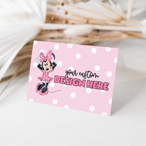 May include: A pink card with white polka dots and the text "your custom DESIGN HERE". The card features a cartoon image of Minnie Mouse in a pink dress and bow. The background includes dried plants.