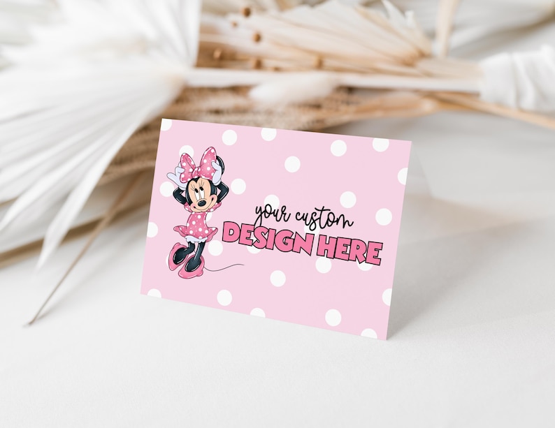 May include: A pink card with white polka dots and the text "your custom DESIGN HERE". The card features a cartoon image of Minnie Mouse in a pink dress and bow. The background includes dried plants.