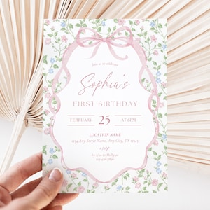 May include: A first birthday invitation with a floral design and a pink ribbon border. The invitation reads "Sophia's FIRST BIRTHDAY" and the date "FEBRUARY 25". The background is decorated with small pink and blue flowers.