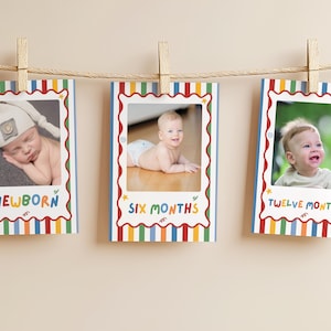 May include: Three rectangular milestone cards hanging from a twine string with wooden clothespins. Each card features a colorful vertical striped border and a scalloped frame. The cards display the text NEWBORN, SIX MONTHS, and TWELVE MONTHS.