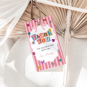 Può includere: Un'etichetta regalo rettangolare con sfondo a righe rosa e bianche, caratterizzata da un centro smerlato bianco con il testo Thank You, FOR CELEBRATING WITH ME!, e love. Penelope. L'etichetta è decorata con icone colorate di stelle, farfalle e gemme.