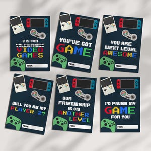 May include: Six navy blue Valentine's Day cards with gaming themes. Each card features a pixelated design of a game controller, handheld console, and text like "You've Got Game" and "I'd Pause My Game For You".