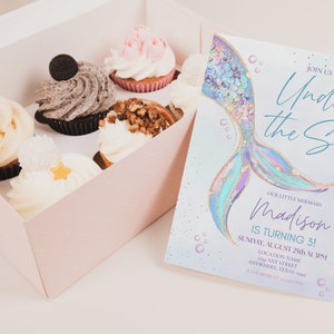 May include: A pastel blue and purple mermaid tail with gold glitter accents on a light blue background with white bubbles. The text "Join us Under the Sea" is written in a blue script font. The text "Our Little Mermaid Madison is turning 3!" is written in a black font. The text "Sunday, August 25th at 3PM" is written in a black font. The text "Location Name Any Street Anywhere, Texas" is written in a black font.