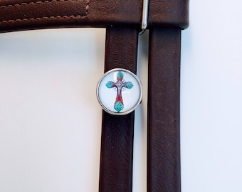 May include: Two brown leather straps with a silver buckle and a round, white, silver-rimmed charm with a red and turquoise cross design.