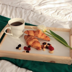 Holz-Frühstückstablett mit klappbaren Beinen auf dem Bett, serviert mit Kaffee, Croissant und kleinen Frühstückssnacks.