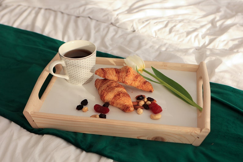 Holz-Frühstückstablett mit klappbaren Beinen auf dem Bett, serviert mit Kaffee, Croissant und kleinen Frühstückssnacks.