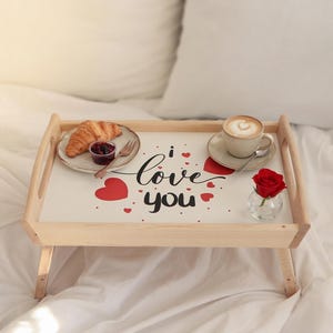 Frühstückstablett mit Love-You-Schriftzug, roten Herzen, Kaffee und Gebäck als romantisches Frühstück im Bett.