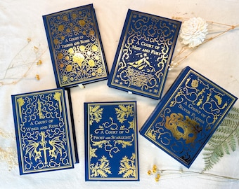 May include: Five blue hardback books with gold foil lettering and designs. The titles are "A Court of Thorns and Roses", "A Court of Mist and Fury", "A Court of Wings and Ruin", "A Court of Frost and Starlight", and "A Court of Silver Flames".