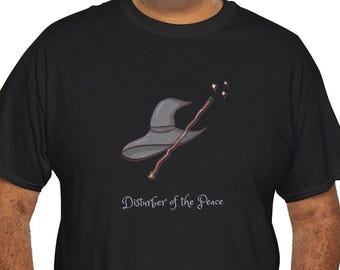Op de afbeelding: Een zwart T-shirt met korte mouwen en een afbeelding van een grijze puntige tovenaarshoed en een bruine toverstaf met kleine gele vonkjes aan de punt. Onder de afbeelding staat de tekst "Disturber of the Peace" in een wit cursief lettertype.