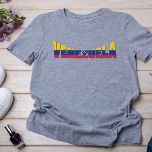 May include: A gray t-shirt with the word "VENEZUELA" printed on it in yellow, blue, and red, the colors of the Venezuelan flag.