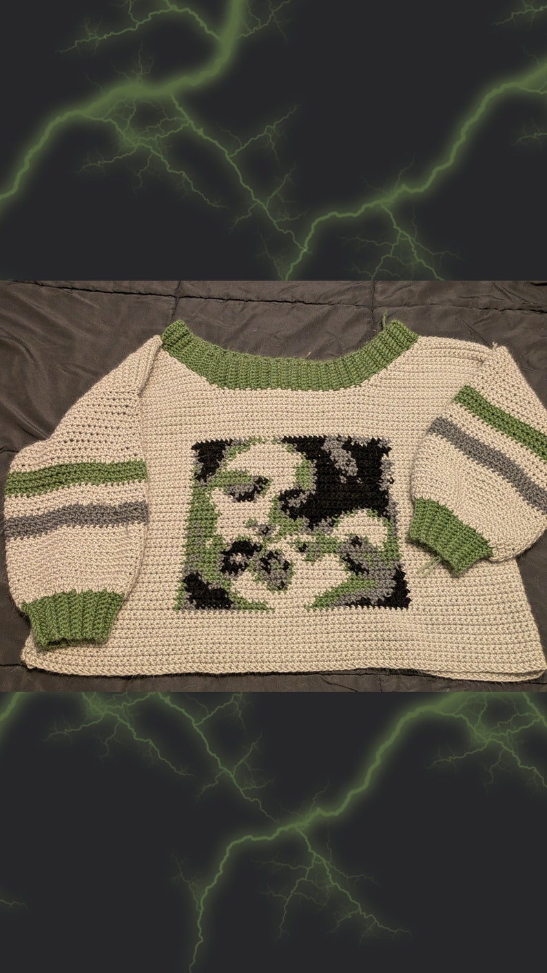 May include: A crocheted sweater with a green, black and grey geometric design on the front. The sweater has green and grey stripes on the sleeves and a green neckline.