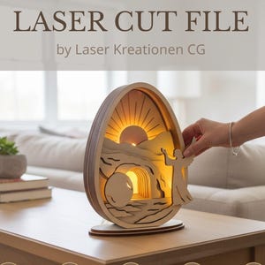 Könnte beinhalten: Eine hölzerne Laserdatei in Eiform mit einem geschichteten Design, das einen Sonnenaufgang und einen Engel darstellt. Der Text "LASER CUT FILE" und "Instant Download" sind sichtbar. Das Produkt steht auf einem Holztisch.