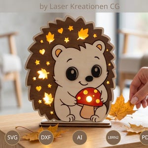 May include: A laser-cut wooden hedgehog lamp featuring cutouts of stars, leaves, and hearts, with a mushroom graphic. The design includes text reading LASER CUT FILE by Laser Kreationen CG, Instant Download, and file formats SVG, DXF, AI, LBRN2, and PDF.