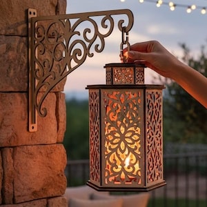 Pode incluir: Uma lanterna hexagonal de madeira com padrões florais intrincados cortados a laser e um brilho interno quente, suspensa num suporte de parede de metal decorativo com volutas. A lanterna é castanho-clara e emite uma luz laranja suave.