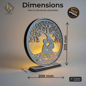 Puede incluir: Un expositor circular de madera iluminado con una silueta de &aacute;rbol cortada a l&aacute;ser y una figura de padre e hijo. El texto dice "Mama" y "Wurzeln meines Herzens". Las dimensiones son 205 mm de alto, 200 mm de ancho y 45 mm de profundidad.