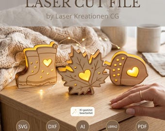 May include: Three laser-cut wooden light decorations featuring a rain boot, a maple leaf, and an acorn, each with a heart-shaped cutout. The text LASER CUT FILE by Laser Kreationen CG is visible, along with file format icons SVG, DXF, AI, LBRN2, and PDF.