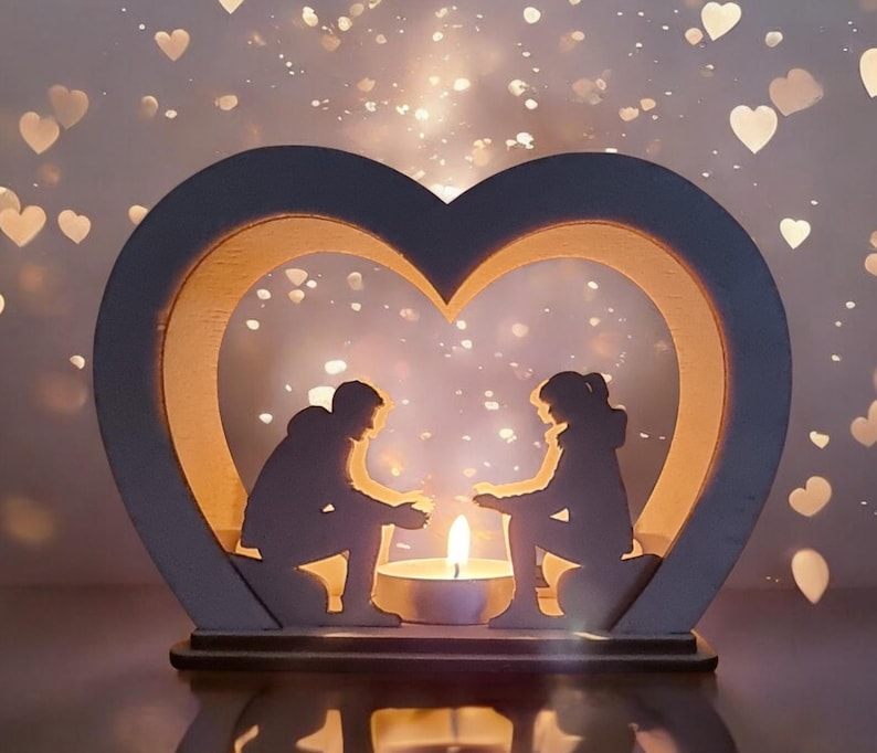 May include: A wooden heart-shaped candle holder with two silhouettes of people inside. The candle holder is lit with a small candle in the center.