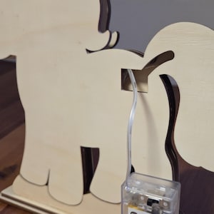 K&ouml;nnte beinhalten: Eine Holz-Pony-f&ouml;rmige Leuchte. Das Pony besteht aus hellfarbenem Holz mit dunkelbraunen Akzenten. Ein klarer Draht erstreckt sich vom Pony zu einer kleinen, durchsichtigen Plastikbox. Das Pony steht auf einem rechteckigen Sockel.