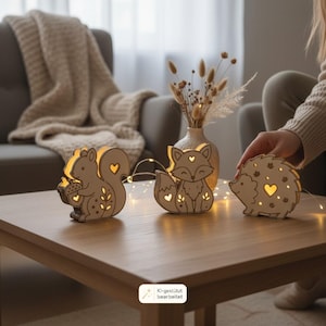 May include: Three light-up wooden animal figures shaped like a squirrel holding an acorn, a fox, and a hedgehog. Each light-colored wooden cutout features heart-shaped and leaf-patterned cutouts that glow with warm internal LED light.