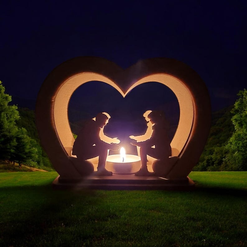 May include: A wooden heart-shaped candle holder with two silhouettes of people holding hands inside. The candle holder is lit with a warm glow, creating a romantic ambiance.