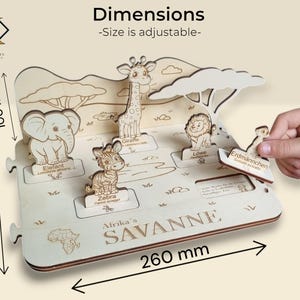 Op de afbeelding: Een houten puzzel met Afrikaanse dieren, waaronder een olifant, een giraffe, een zebra en een leeuw. De puzzel is ongeveer 26 cm breed, 20 cm lang en 10 cm hoog. De tekst "Afrika's SAVANNE" is zichtbaar.