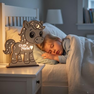 K&ouml;nnte beinhalten: Ein Nachtlicht aus Holz in Form eines Cartoon-Pferdes mit den Worten "Gute Nacht" und einem Herz. Das Pferd hat einen Mond und Sterne. Das Licht steht auf einem wei&szlig;en Nachttisch.