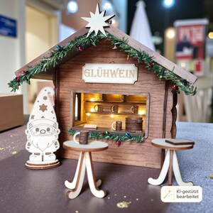 May include: A miniature wooden Gl&uuml;hwein stall featuring a brown structure with a white star on the roof, green garland with colorful lights, and a sign reading GL&Uuml;HWEIN. Includes a gnome figure and two small round tables with tiny mugs.