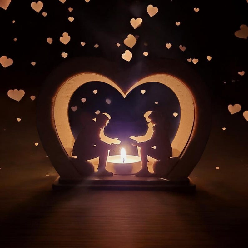 May include: A wooden heart-shaped candle holder with two silhouettes of people holding hands inside. The candle holder is lit with a small candle in the center.