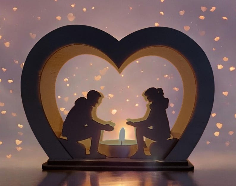 May include: A wooden heart-shaped candle holder with two silhouettes of people sitting inside. The candle holder is lit and the light shines through the silhouettes. The background is a soft purple with white dots.