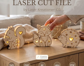 May include: Three light-colored wooden animal figures including a squirrel holding an acorn, a fox, and a hedgehog. Each figure features cut-out heart and leaf shapes that emit a warm glow. Text reads LASER CUT FILE by Laser Kreationen CG.