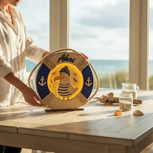 Pu&ograve; includere: Lampada decorativa a tema nautico a forma di salvagente, con un gabbiano dei cartoni animati con cappello e camicia a righe. La lampada &egrave; blu e beige, con la scritta "Ahoi" in alto. Ancore decorative sui lati.