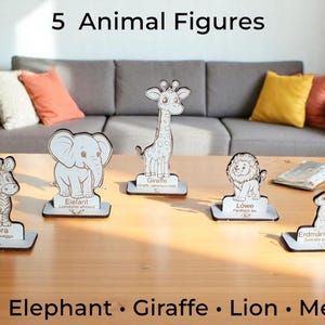 Op de afbeelding: Houten dierenfiguren van een zebra, olifant, giraf, leeuw en stokstaartje. Elke figuur staat op een kleine basis met de naam van het dier. De tekst "5 Animal Figures" staat bovenaan.