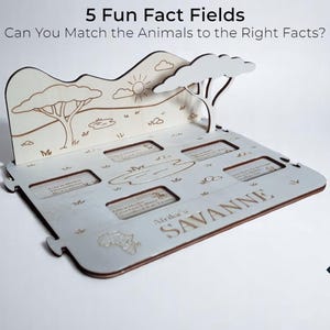 Op de afbeelding: Een lasergesneden houten educatief spel met de tekst "5 Fun Fact Fields". Het spel toont een savanne-sc&egrave;ne met een boom, zon en wolken. Het bevat vakken voor het matchen van dierlijke feiten, met de woorden "Africa's Savanne".