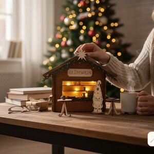 May include: A wooden miniature stall with a sign reading GL&Uuml;HWEIN, featuring interior warm lighting, a star topper, and a small gnome figure. Two tiny round tables are placed in front of the structure, which is crafted from brown wood.